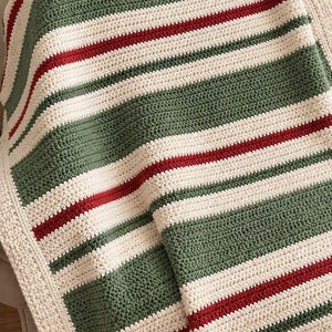 May include: A crocheted blanket featuring horizontal stripes in cream, sage green, and deep red. The textile has a consistent, textured stitch pattern throughout, with a wide cream-colored border framing the striped design on all sides.