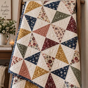 May include: A quilted blanket featuring a geometric pattern of triangles. The design consists of alternating cream-colored triangles and various floral-patterned triangles in shades of mustard yellow, navy blue, sage green, and deep red.