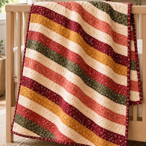 Puede incluir: Una colcha rectangular con rayas diagonales en colores alternos de rojo oscuro, amarillo mostaza, verde bosque y crema. Cada franja está decorada con un pequeño patrón floral repetitivo. La colcha tiene un borde de tela de color rojo oscuro.