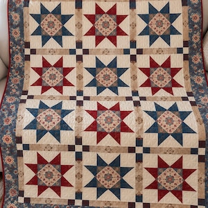 May include: A quilt featuring a repeating pattern of nine star blocks in alternating red and blue colors. Each star block contains a central floral print square. The quilt is bordered by a blue floral fabric and a thin red binding edge.