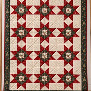 May include: A rectangular quilt featuring a repeating star pattern in deep red, forest green, and cream. The design includes holly leaf motifs and a dark green border decorated with small gold-coloured pine tree icons throughout the fabric.