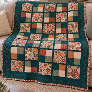 May include: A patchwork quilt featuring a grid of alternating squares. The design includes solid blocks in shades of teal, mustard yellow, and rust red, interspersed with floral and fern-patterned fabric squares in matching earth tones.