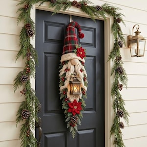 May include: A hanging gnome decoration featuring a tall red and green plaid hat, a cream-colored knit beard, and a small lantern. The gnome is adorned with red poinsettia flowers, pinecones, and berries, suspended on a dark door with a pine garland.