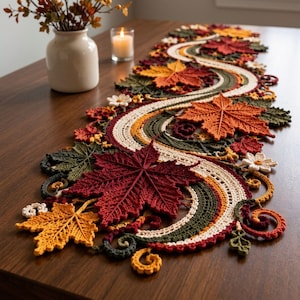 Könnte beinhalten: Ein gehäkelter Tischläufer mit einem geschwungenen Design aus Herbstblättern in den Farben Dunkelrot, Orange, Gelb und Olivgrün. Der Läufer enthält detaillierte Blattmuster, kleine weiße Blüten und geschwungene Rankenverzierungen.