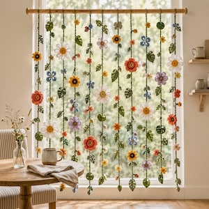 May include: A decorative window hanging featuring multiple vertical strands of crocheted green vines adorned with various colorful flowers and leaves. The flowers include white daisies, orange blossoms, yellow sunflowers, and purple blooms.