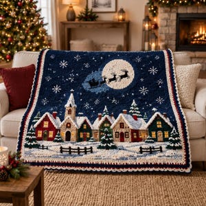 May include: A dark blue crochet blanket featuring a winter village scene with snow-covered houses, a church, and evergreen trees. Above the village, a large white moon silhouettes Santa Claus and his reindeer sleigh against a starry night sky.