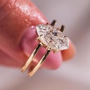Puede incluir: Un anillo de oro con una piedra preciosa transparente de corte marquesa en un engaste de cuatro garras. La banda es fina y está hecha de oro amarillo pulido, mostrando un diseño sencillo que resalta el brillo de la piedra facetada.