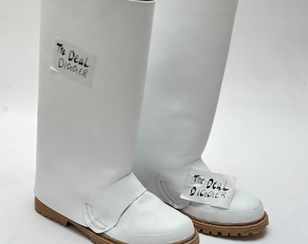 May include: A pair of tall white boots with a smooth finish, featuring a brown lug sole and a strap across the vamp. Each boot has a white rectangular label attached with the black handwritten text The Deal DIGGER visible on the surface.