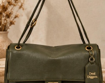 May include: An olive green shoulder bag with a textured finish, featuring a gold-toned rectangular turn-lock closure, matching gold hardware, and a hanging luggage tag embossed with the text Deal Diggers. The bag has two adjustable shoulder straps.