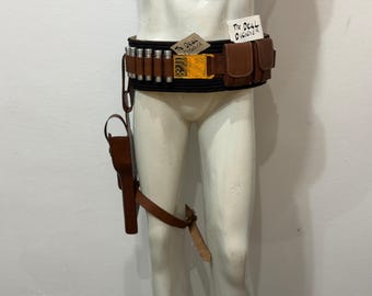 May include: A brown leather utility belt featuring a series of silver cylindrical canisters, a rectangular gold-colored buckle with circuit board patterns, and two attached pouches. A matching holster hangs from the belt with a leg strap attached.