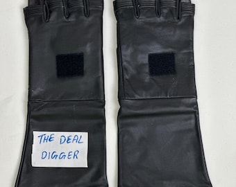 May include: A pair of black leather gauntlet-style gloves featuring long cuffs, ribbed detailing at the knuckles, and a square hook-and-loop fastener patch on the back of each hand. A white rectangular label with the text THE DEAL DIGGER is attached.
