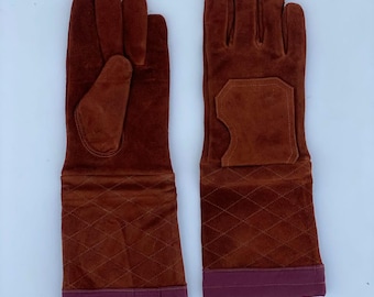 May include: A pair of long, rust-colored suede gloves featuring a quilted diamond pattern on the forearm section and a solid, smooth suede cuff at the wrist. The gloves include a reinforced palm patch and a dark maroon band at the bottom edge.