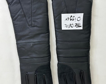 May include: A pair of long black leather gloves featuring a gauntlet-style cuff, ribbed detailing at the wrist, and suede palm patches. A white rectangular paper tag with the handwritten text The DEAL Digger is placed on the right glove.