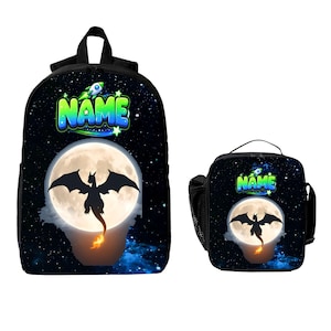 May include: A black backpack and a matching lunch bag featuring a space-themed design with a full moon, a silhouette of a dragon with a flaming tail, and a rocket ship graphic above the word NAME in bright green and blue lettering.