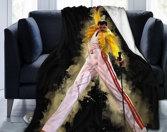 May include: A soft throw blanket featuring a graphic print of a performer in a yellow military-style jacket, white trousers with red side stripes, and a white tank top, holding a microphone stand against a black and gold watercolor background.