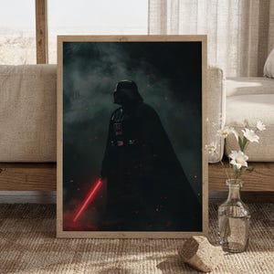 Könnte beinhalten: Ein gerahmter vertikaler Kunstdruck, der Darth Vader in einer dunklen, atmosphärischen Umgebung inmitten von Rauch und Glut zeigt. Die Figur trägt eine schwarze Rüstung und einen wehenden Umhang und hält ein leuchtend rotes Lichtschwert.