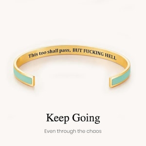 May include: A gold-toned cuff bracelet featuring a light blue enamel inlay along the outer edges. The interior surface is engraved with the black text: This too shall pass, BUT FUCKING HELL. Below the bracelet, the text reads: Keep Going Even through the chaos.