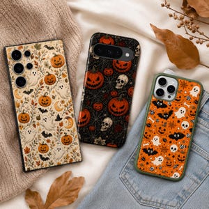 May include: Three smartphone cases featuring Halloween-themed patterns. The left case has a cream background with ghosts, pumpkins, and leaves. The middle case is black with jack-o'-lanterns, skulls, and spiderwebs. The right case is orange with bats, ghosts, and skulls.