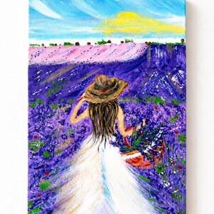 May include: An acrylic painting on canvas depicting a figure from behind, wearing a wide-brimmed straw hat and a long white dress, walking through a vibrant purple lavender field while carrying a basket filled with freshly picked lavender flowers.