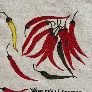 May include: A beige fabric surface featuring a hand-painted illustration of several chilli peppers in shades of red, yellow, and dark green. The peppers are arranged in a cluster and individually, with the black text "WOW CHILLI PEPPERS" printed below.