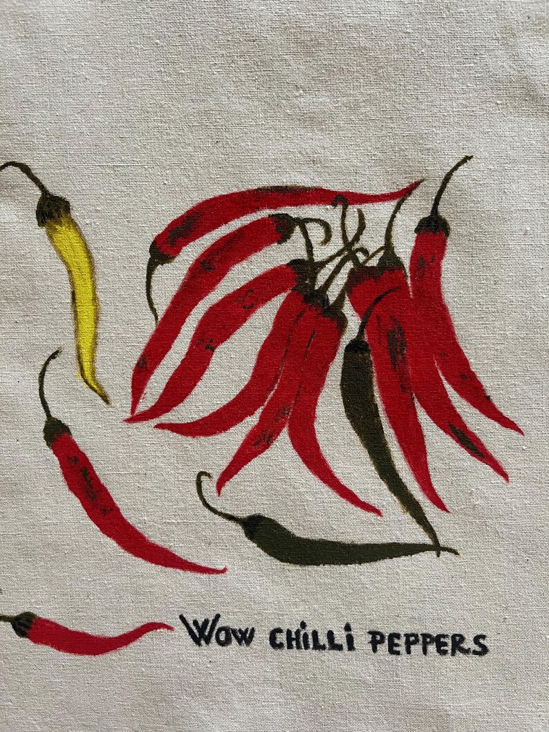 May include: A beige fabric surface featuring a hand-painted illustration of several chilli peppers in shades of red, yellow, and dark green. The peppers are arranged in a cluster and individually, with the black text "WOW CHILLI PEPPERS" printed below.