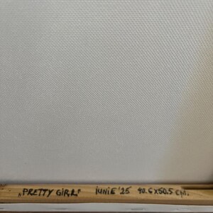 Peut inclure: Une toile blanche tendue sur un cadre en bois. Le cadre en bois pr&eacute;sente une inscription manuscrite noire indiquant : "PRETTY GIRL" JUNIE '25 40.6X50.5 CM. La toile poss&egrave;de une texture tiss&eacute;e visible et est fix&eacute;e sur une structure en bois clair.