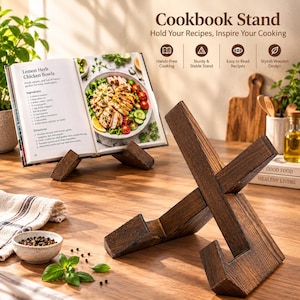May include: A dark brown wooden cookbook stand with an X-shaped design, featuring two interlocking pieces that form a ledge for holding books. The stand is displayed alongside an open cookbook showing a recipe for Lemon Herb Chicken Bowls.