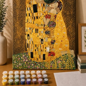 Könnte beinhalten: Ein Malen-nach-Zahlen-Set mit einem Leinwanddruck von Gustav Klimts Der Kuss, vierundzwanzig nummerierten Farbtöpfen in verschiedenen Farben und drei Pinseln mit blauem Griff. Die Leinwand zeigt ein Paar in goldfarbenen Gewändern.
