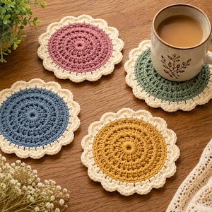 May include: Three round, crocheted coasters in dusty rose, slate blue, and mustard yellow, each featuring a cream-colored scalloped border. A ceramic mug with a brown botanical print sits on a green coaster, matching the set's circular design.