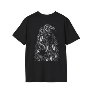 Puede incluir: Una camiseta negra de manga corta con una ilustración gráfica blanca en la parte posterior. El diseño muestra a una persona con el pelo largo y ondulado adornado con plumas y cuentas, con una serpiente enroscada alrededor de la cabeza y los hombros.