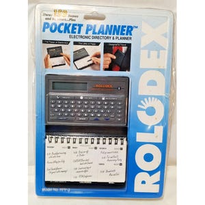 May include: A Rolodex Pocket Planner electronic directory and planner in original blister packaging. The device features a QWERTY keyboard, a digital display, and a spiral-bound paper calendar insert. The packaging includes the text Pocket Planner.