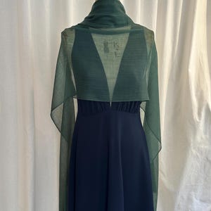 May include: A dark navy blue sleeveless dress with a deep V-neckline and a gathered waist, paired with a sheer, lightweight forest green rectangular shawl draped over the shoulders and around the neck on a dress form.