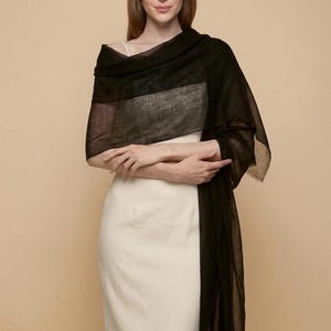 May include: A long, rectangular black shawl made of a lightweight, semi-sheer fabric draped over the shoulders. The shawl features a fine, woven texture and hangs down to the waist, worn over a simple, sleeveless cream-colored dress.