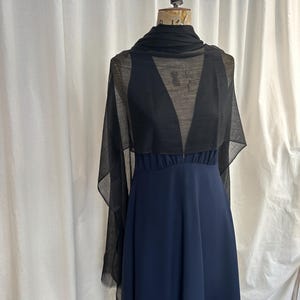 May include: A navy blue sleeveless dress with a gathered waistline and a deep V-neckline, paired with a sheer black rectangular scarf draped over the shoulders and around the neck, displayed on a dress form mannequin.