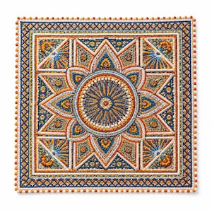 Pode incluir: Uma tapeçaria quadrada de crochê com um padrão central de mandala circular em tons de azul, laranja e branco. O design inclui formas geométricas de estrela, pontos texturizados e uma borda decorativa finalizada com pequenos pompons.