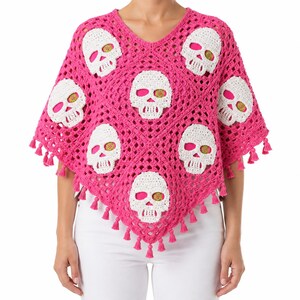 Könnte beinhalten: Ein leuchtend pinkfarbener Häkelponcho mit V-Ausschnitt und einem sich wiederholenden Muster aus weißen Totenkopfmotiven. Das Kleidungsstück ist in einem offenen Häkelstich gefertigt und mit kleinen pinken Quasten am Saum verziert.