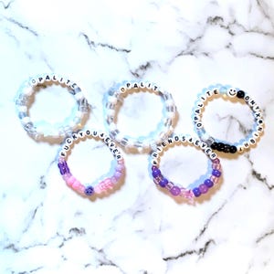 May include: Five beaded bracelets featuring white letter beads and colorful accents. Two bracelets spell OPALITE, one spells FUCKYOU4EVER, one spells FRIENDS4EVER, and one spells OPALITE ONYX NIGHT. The beads include clear, white, pink, purple, and black tones.