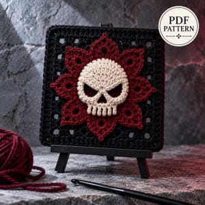 Pode incluir: Um motivo de crochê quadrado com uma caveira cor de creme no centro, rodeada por um design floral vermelho escuro sobre um fundo quadrado preto. O texto PDF PATTERN é visível no canto superior direito da imagem.