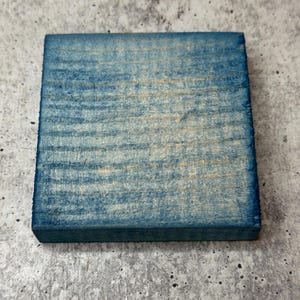 May include: A square piece of wood painted a light blue color. The wood has a natural grain pattern.