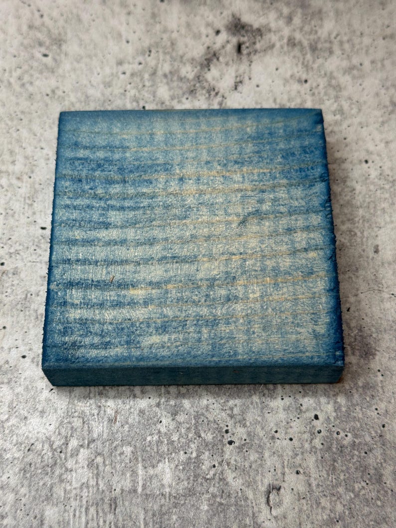 May include: A square piece of wood painted a light blue color. The wood has a natural grain pattern.