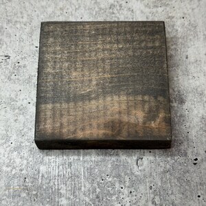 May include: A square piece of wood with a dark brown stain. The wood has a natural grain pattern.