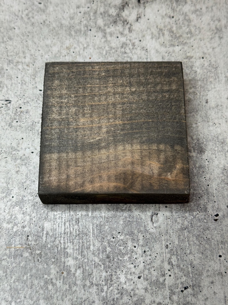 May include: A square piece of wood with a dark brown stain. The wood has a natural grain pattern.
