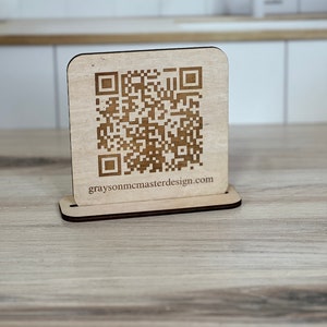 May include: A wooden sign with a QR code and the text "graysonmcmasterdesign.com" printed on it.