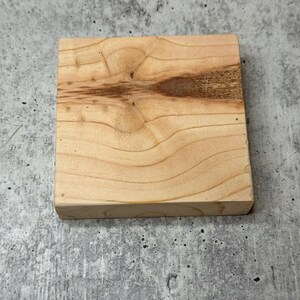 May include: A square piece of unfinished light brown wood with a knot in the centre.