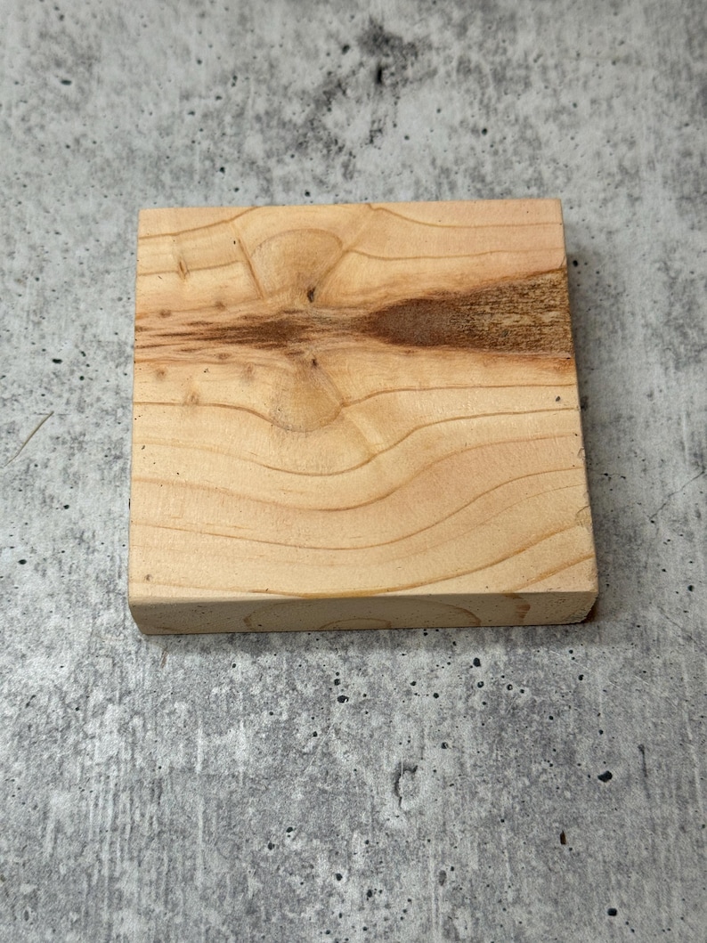 May include: A square piece of unfinished light brown wood with a knot in the centre.