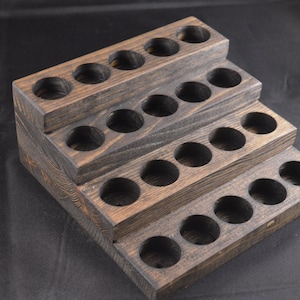 May include: A wooden tiered stand with 20 round holes for storing essential oils or other small bottles. The stand is stained a dark brown colour and has a rustic appearance.