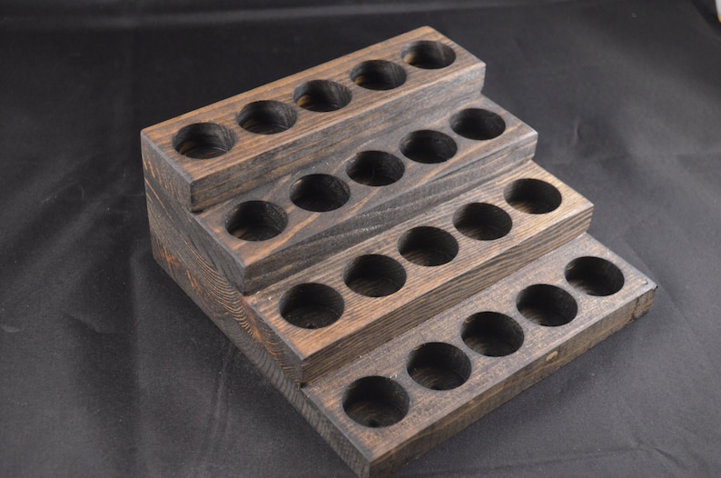 May include: A wooden tiered stand with 20 round holes for storing essential oils or other small bottles. The stand is stained a dark brown colour and has a rustic appearance.
