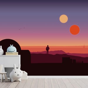 Op de afbeelding: Een witte opbergkast met een kleine houten stoel en een witte lamp in de vorm van een konijn. De muur is voorzien van een muurschildering van een woestijnlandschap bij zonsondergang met twee zonnen en het silhouet van een persoon.