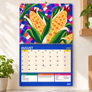 May include: A wall calendar for August 2027 featuring a vibrant illustration of yellow corn cobs with green husks against a colorful mosaic background. The grid displays dates from 1 to 31, with sections for planting, pruning, and harvesting tasks.