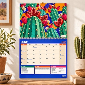 May include: A June 2027 wall calendar featuring a vibrant illustration of green cacti with red fruit against a blue and orange background. The calendar grid displays dates, holidays, and gardening tips for planting, pruning, and harvesting.